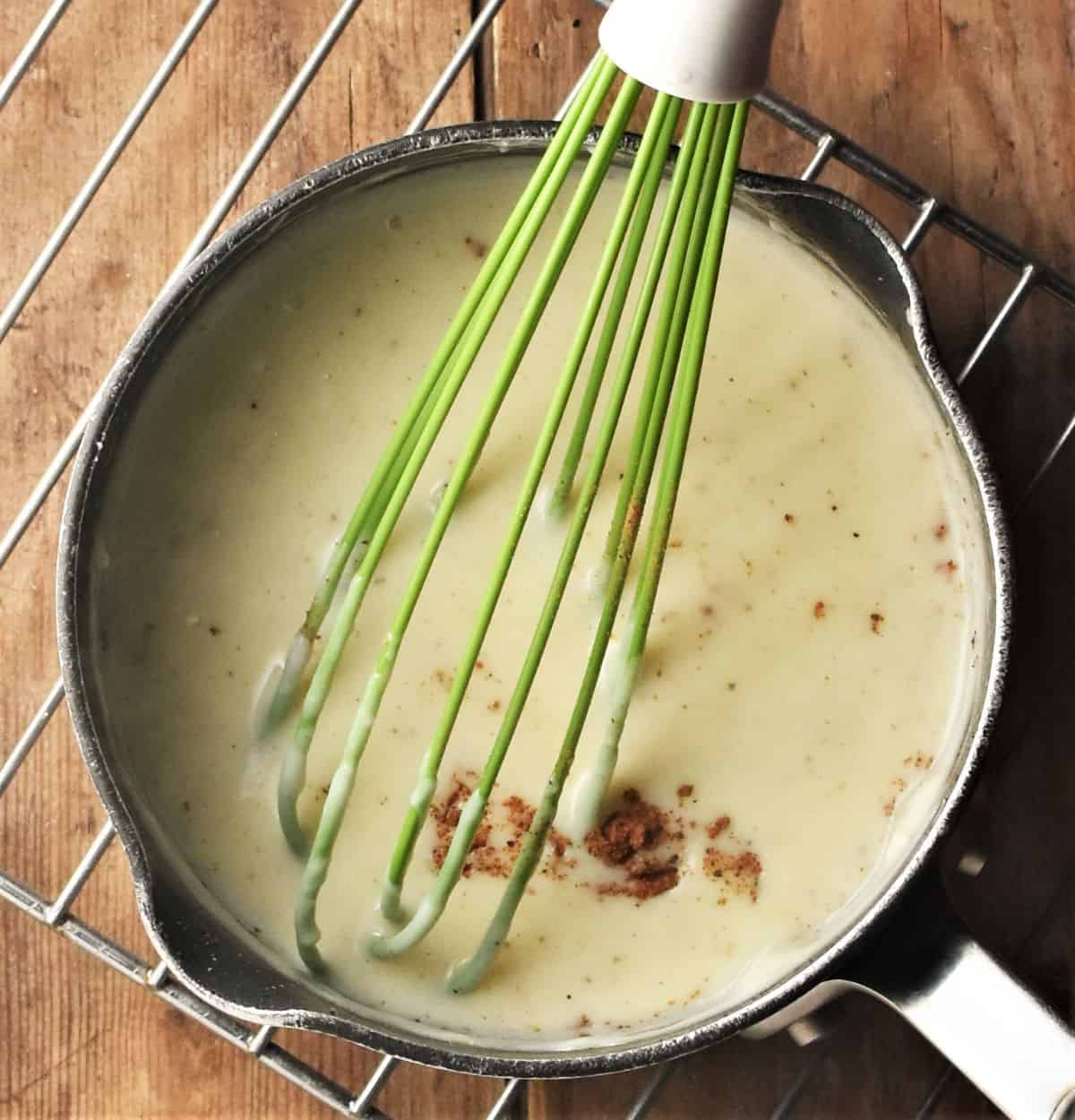 Whisking bechamel sauce in small pan.