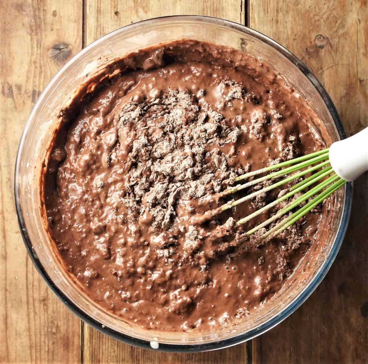 Combining wet and dry ingredients for chocolate muffins in bowl with whisk.