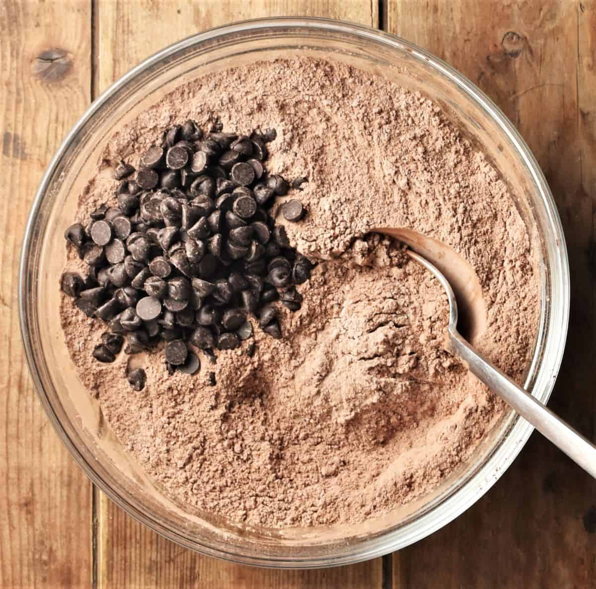 Dry ingredients mixture and chocolate chips in bowl with spoon.