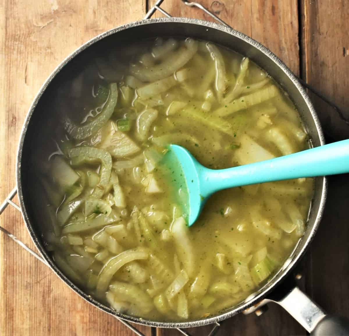Cooking fennel soup in large pot with blue spoon.