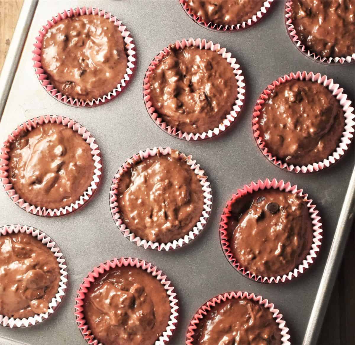 Chocolate muffin batter in paper cases inside muffin pan.