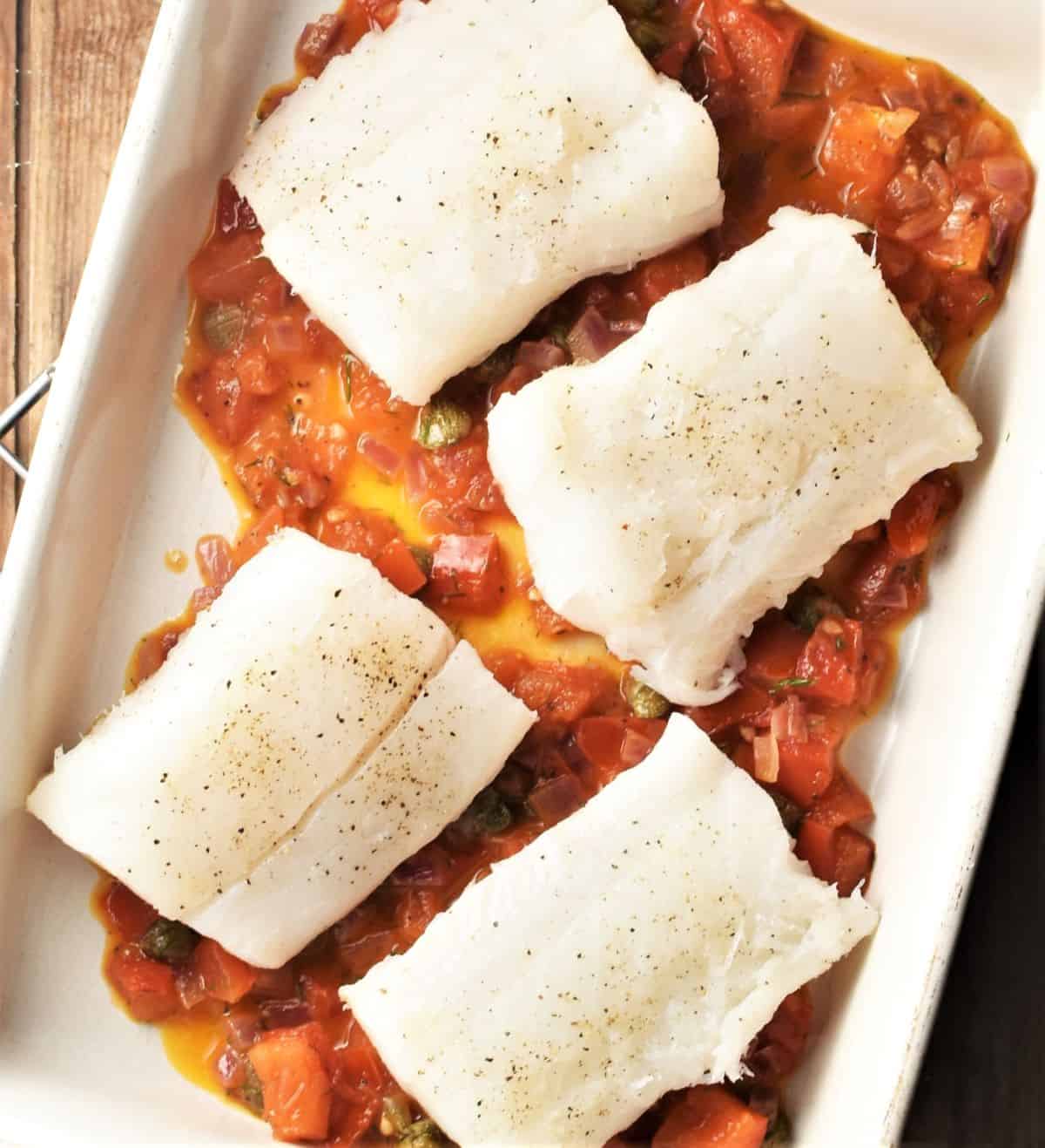 4 pieces of white fish on top of tomato sauce in rectangular dish.