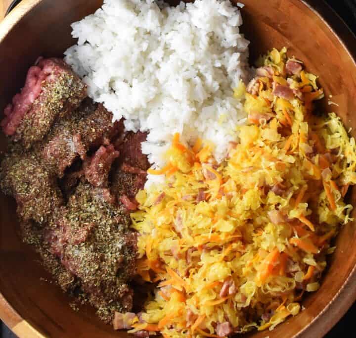 Ground meat with herbs, cooked rice and sauerkraut cabbage roll mixture in wooden bowl.