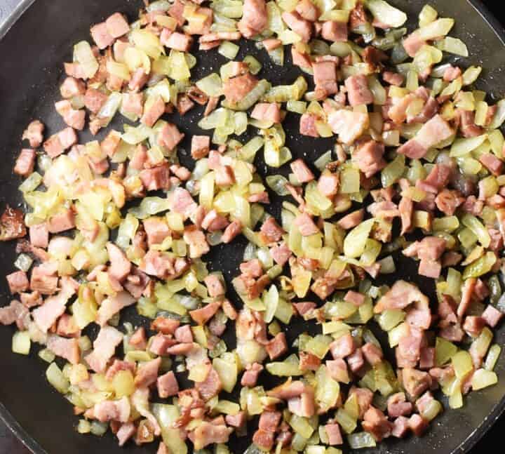 Top down view of chopped bacon and onion in frying pan.
