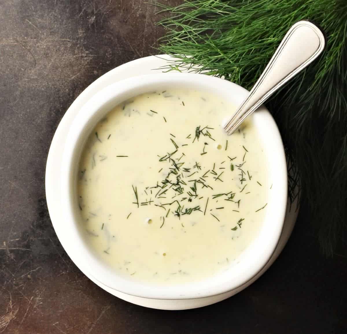 Top down view of dill honey sauce in white bowl with spoon.