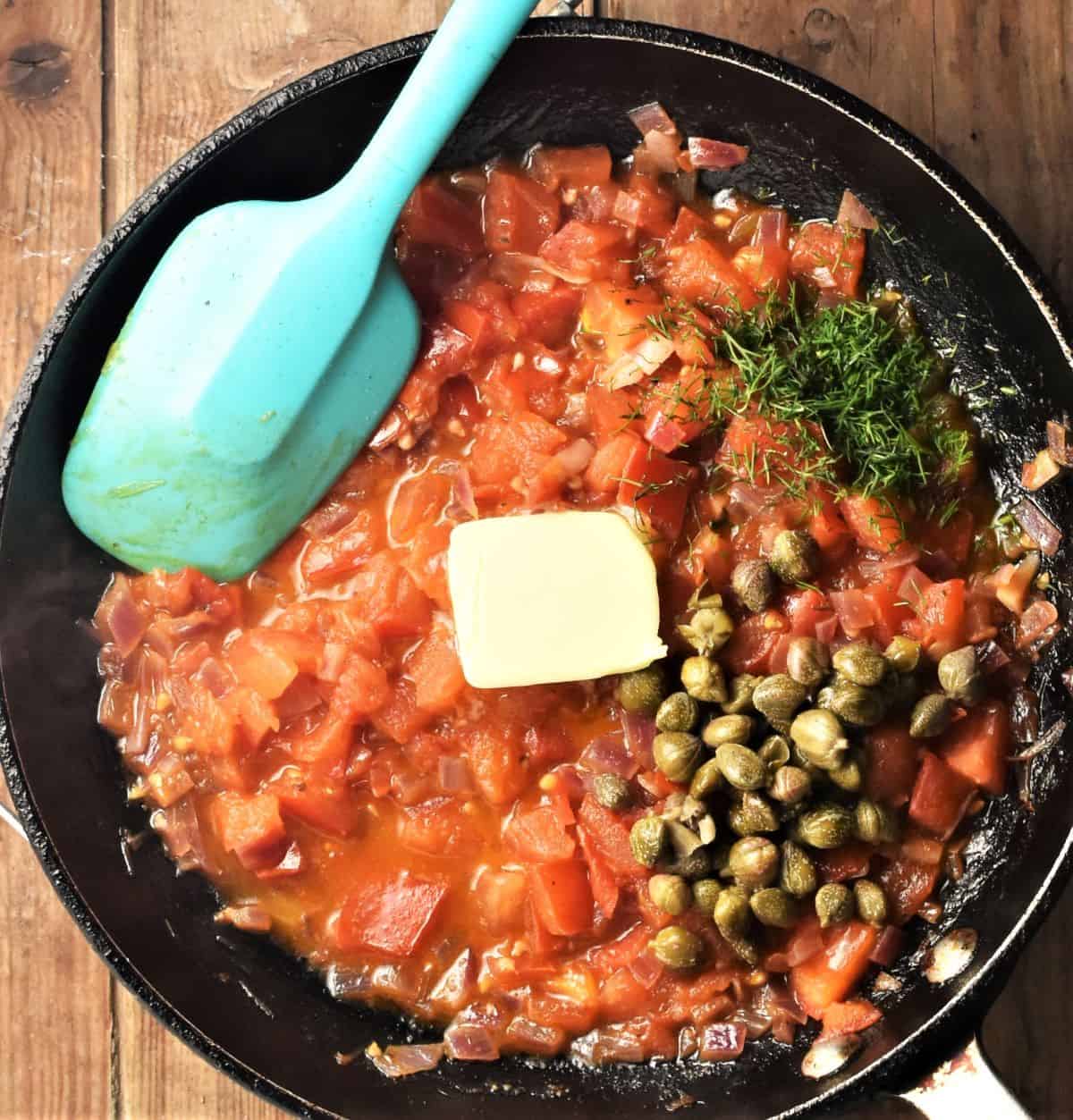 Tomato sauce with capers, dill and butter in pan with blue spoon.