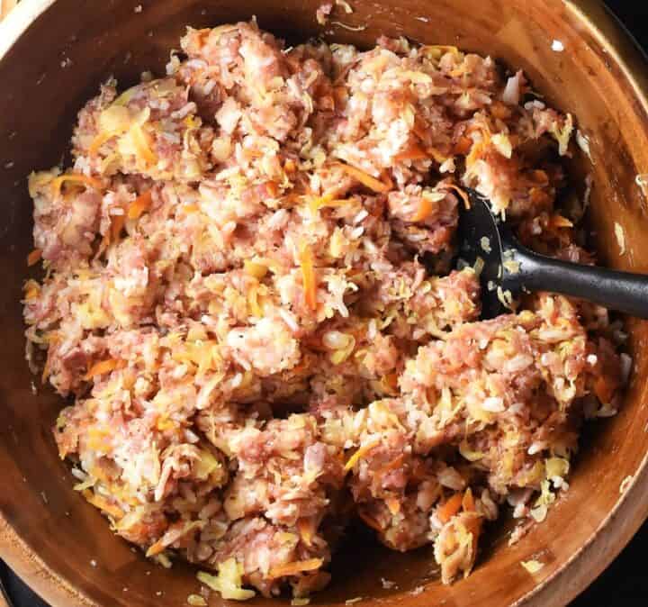 Sauerkraut, meat and rice filling mixture for cabbage rolls in wooden bowl with black spoon.