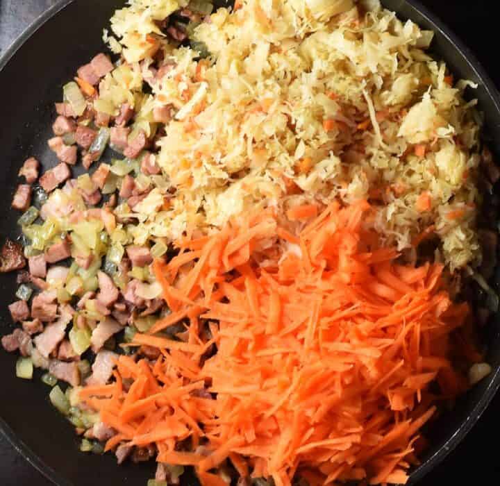 Fried onion and bacon with shredded carrot and chopped sauerkraut in pan.