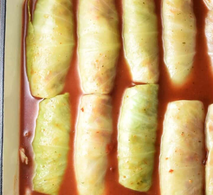 Top down view of unbaked cabbage rolls in tomato sauce in casserole dish.