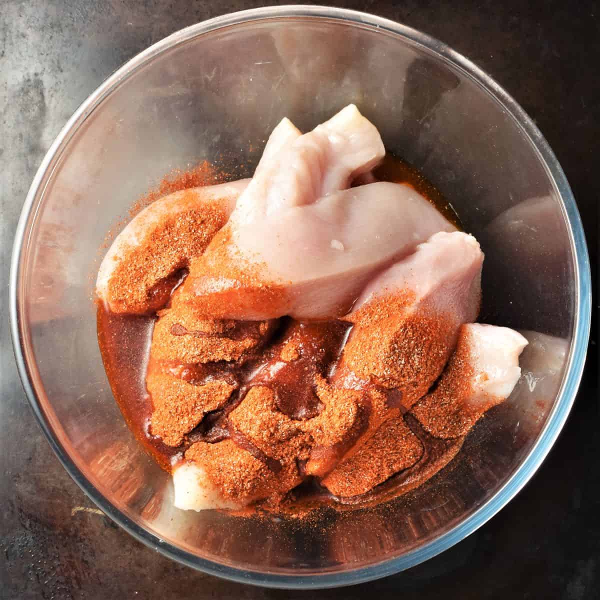 Chicken breast pieces with spices in mixing bowl.