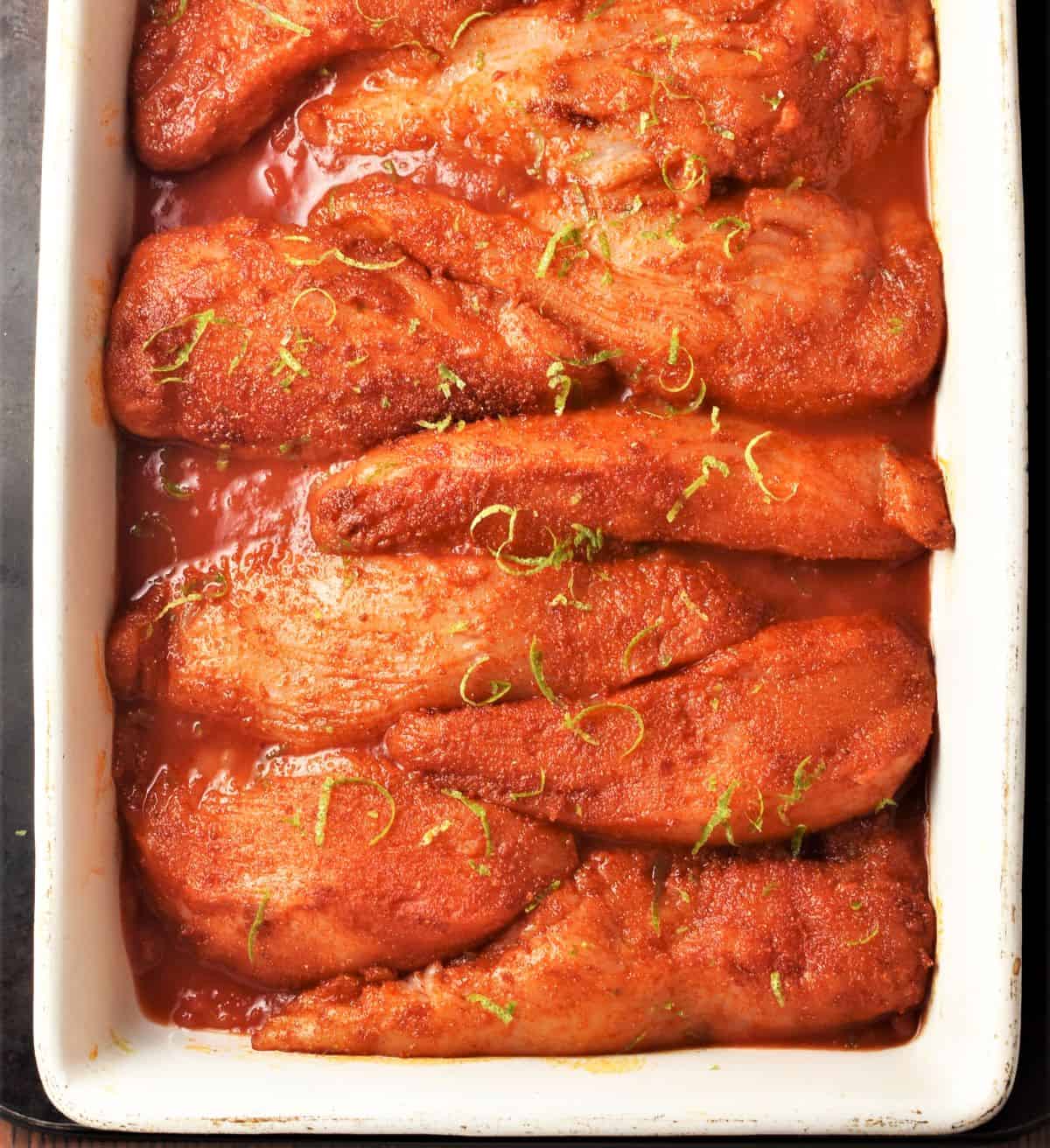 Chicken breast pieces with spices in single layer in casserole dish.