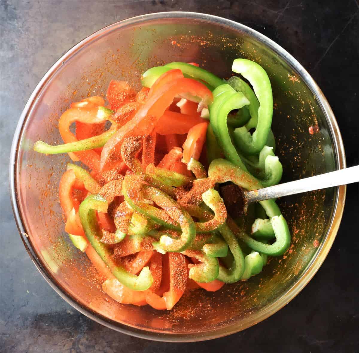 Strips of red and green peppers with spices in bowl with spoon.