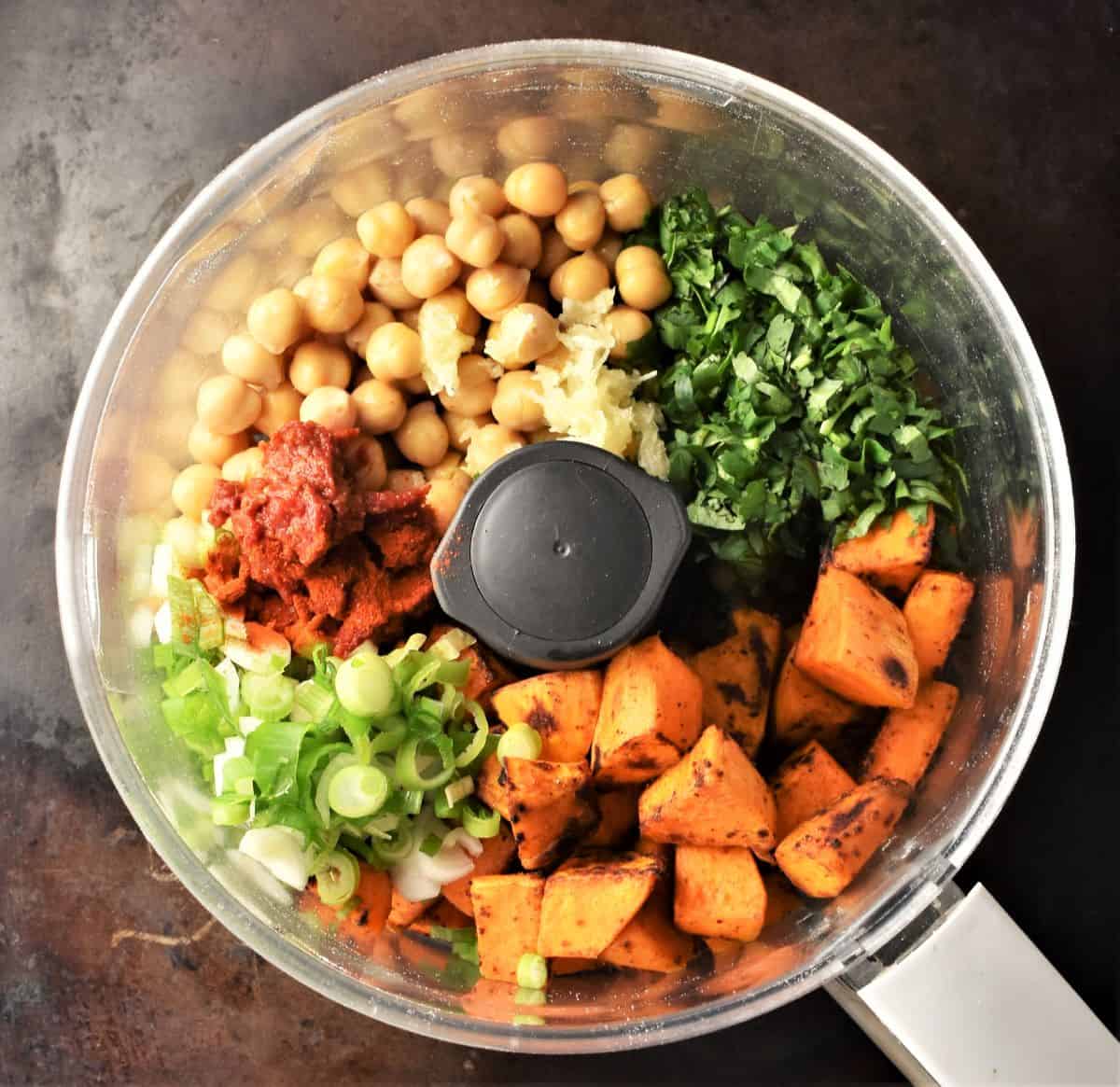 Chunks of sweet potato, chickpeas and herbs in blender bowl.