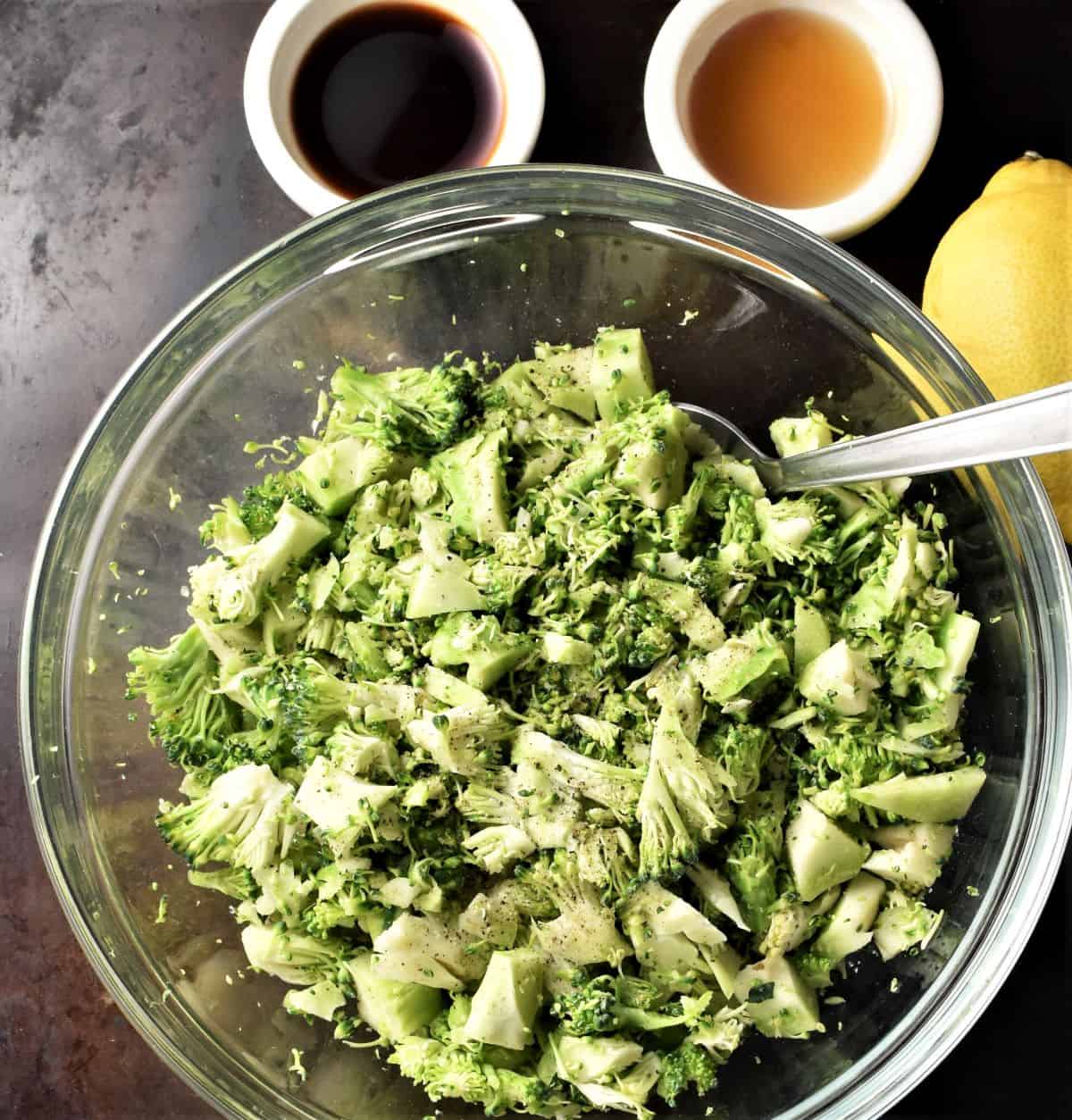 Broccoli pieces in mixing bowl with lemon and sauces in background.