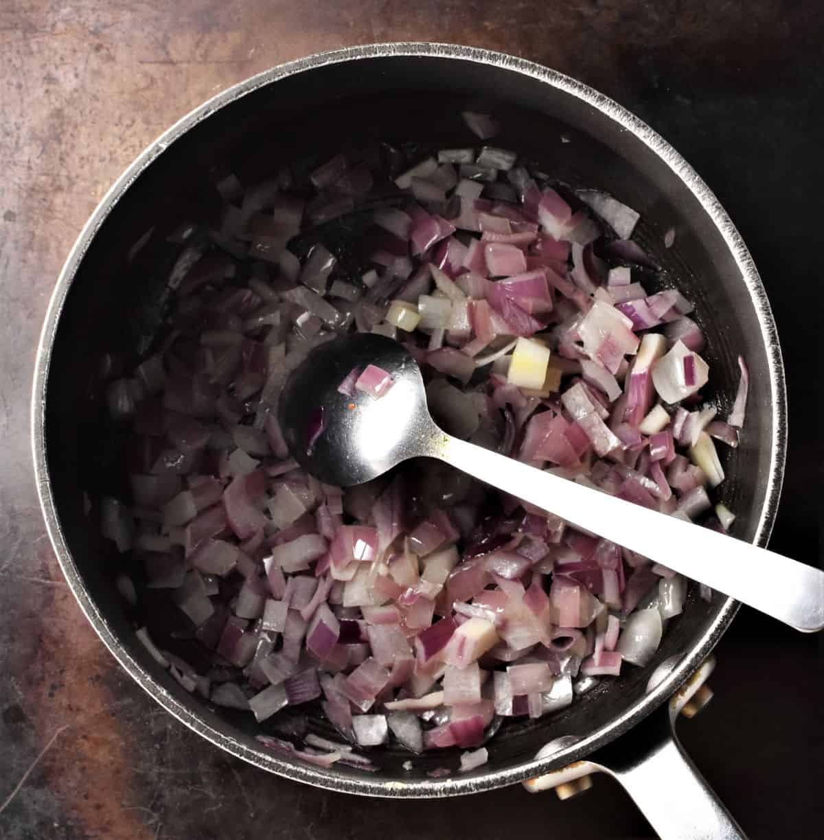 Cooking chopped red onion in pot with spoon.