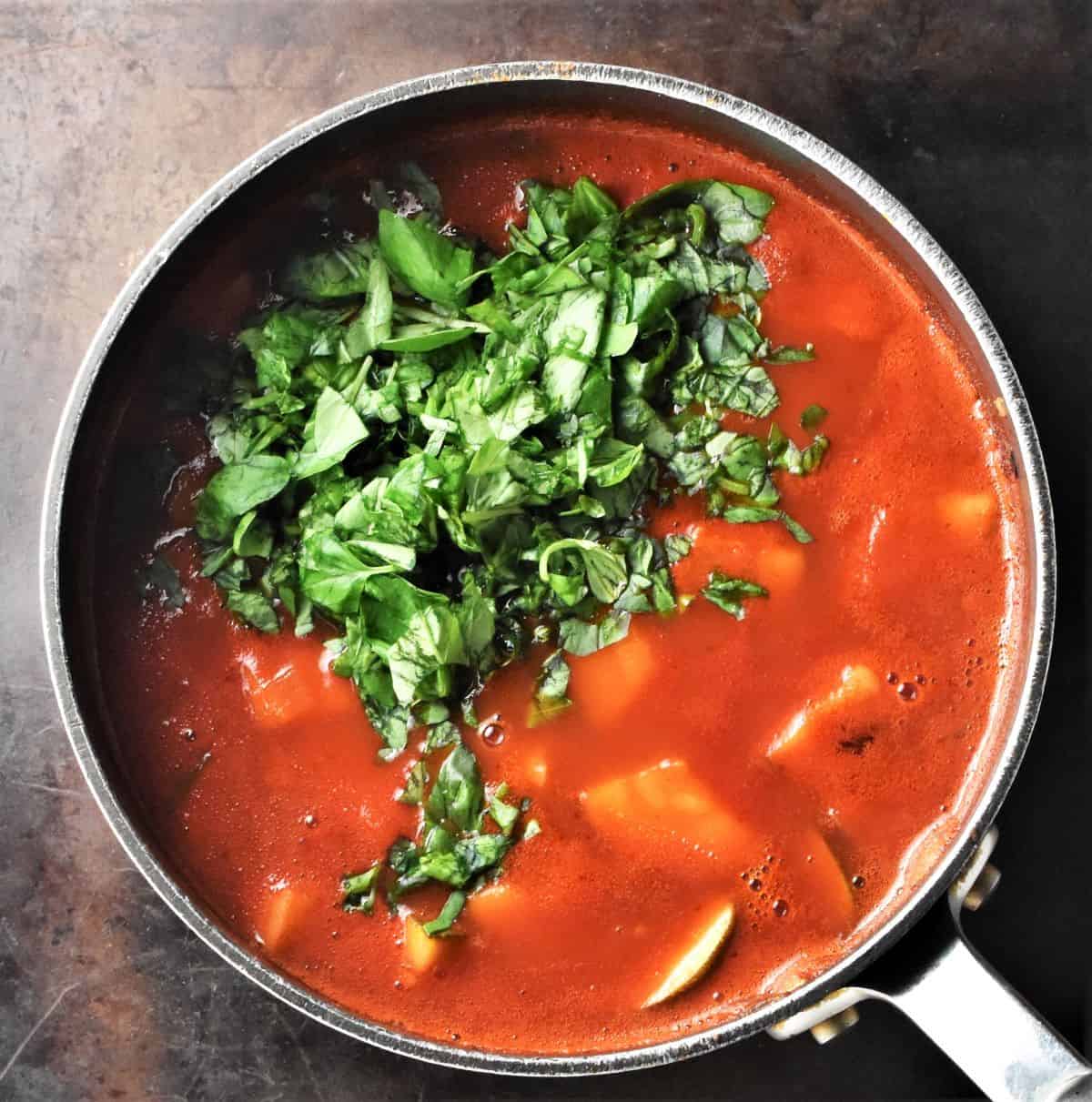 Tomato soup with chunks of zucchini and chopped basil in pot.