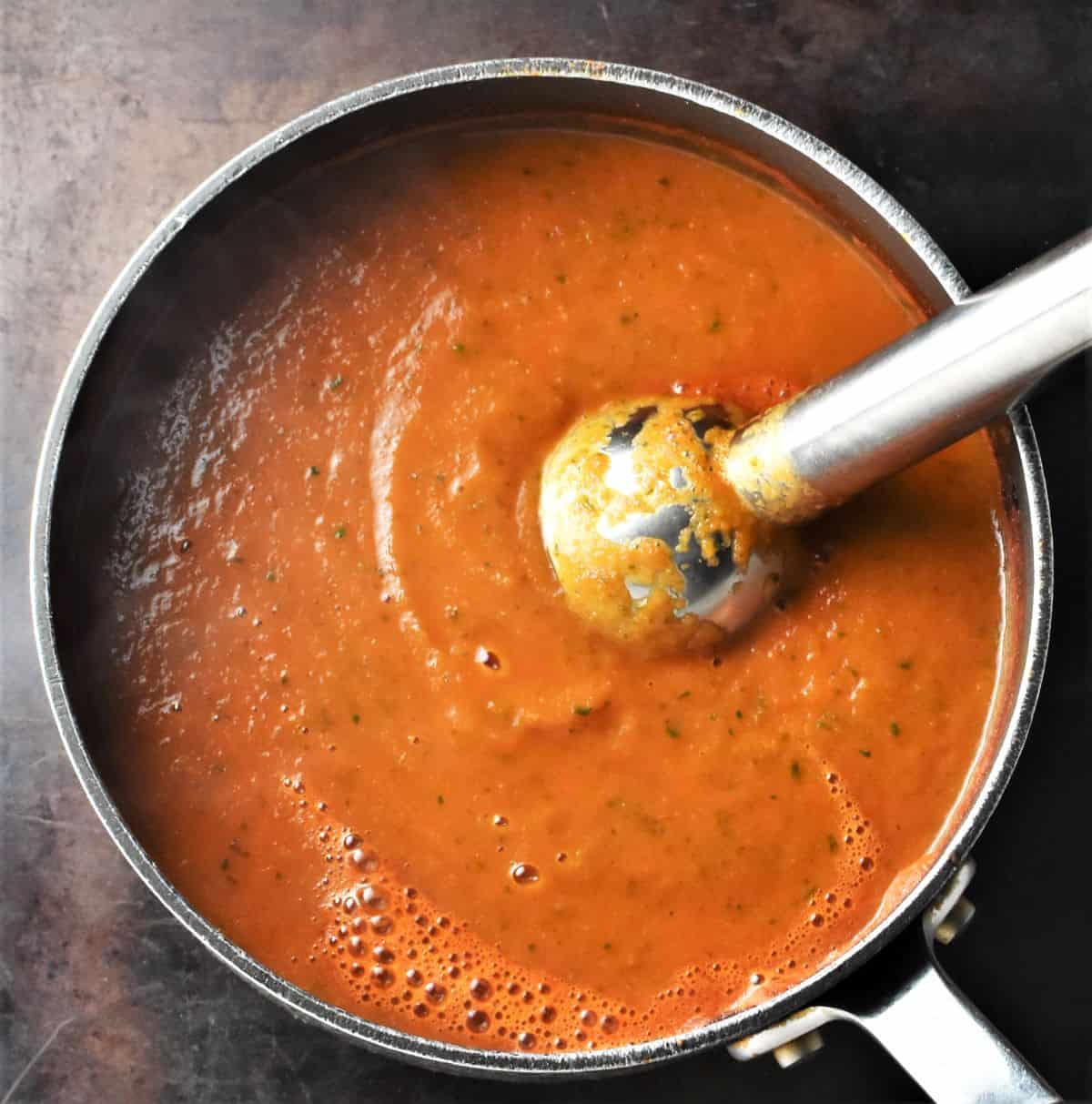 Pureeing tomato and zucchini soup in pot.
