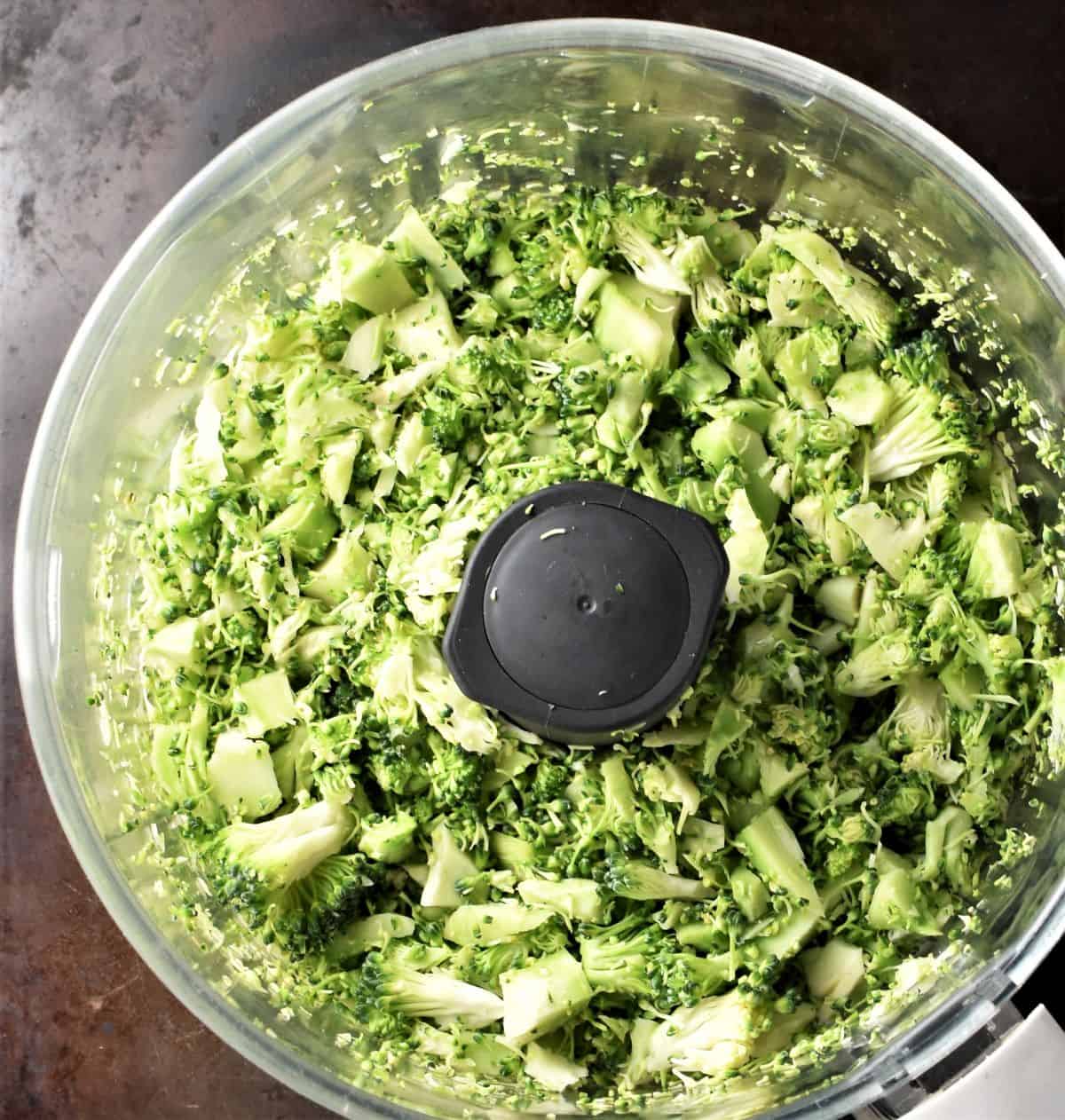 Small pieces of raw broccoli in food processor bowl.
