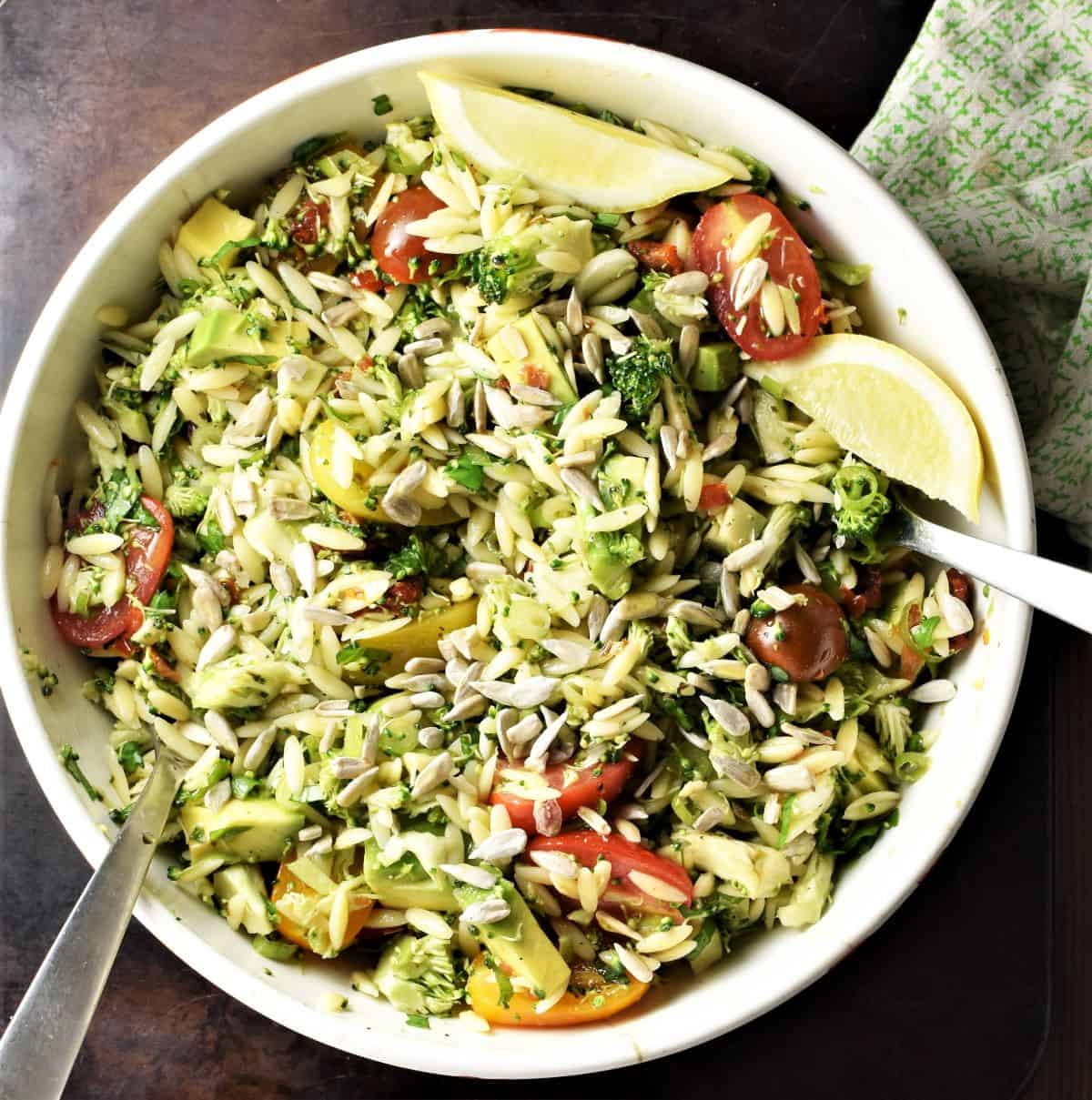 Broccoli and pasta salad with lemon wedges in white bowl with spoons.