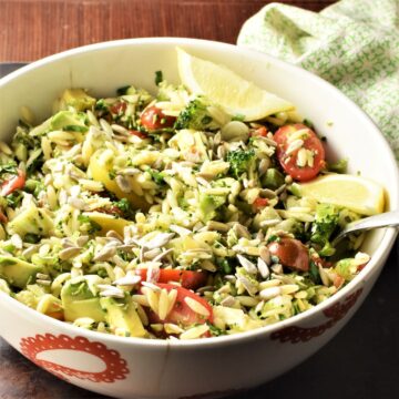 Side view of raw broccoli salad in white bowl with spoon.
