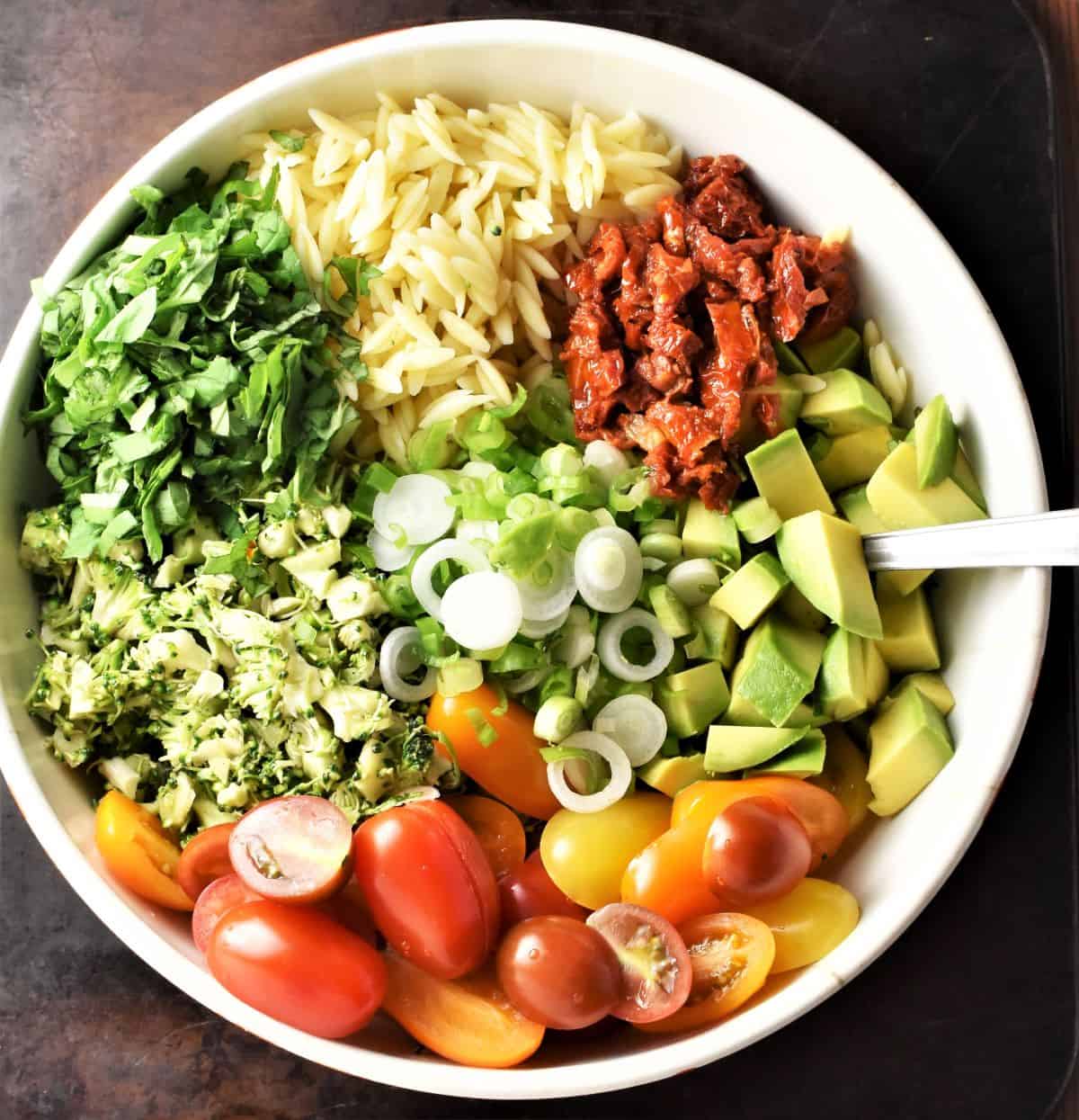 Broccoli and pasta salad ingredients assembled in large white bowl.