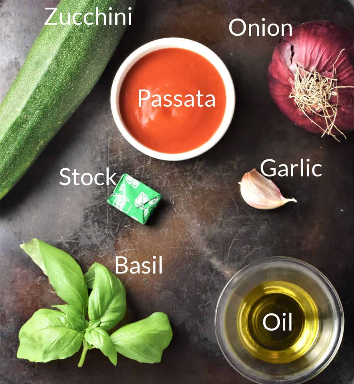 Ingredients for making zucchini tomato soup recipe on top of metal surface.