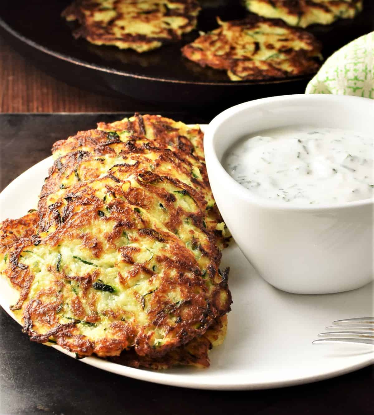 Side view of zucchini fritters on top of plate with yogurt dip.