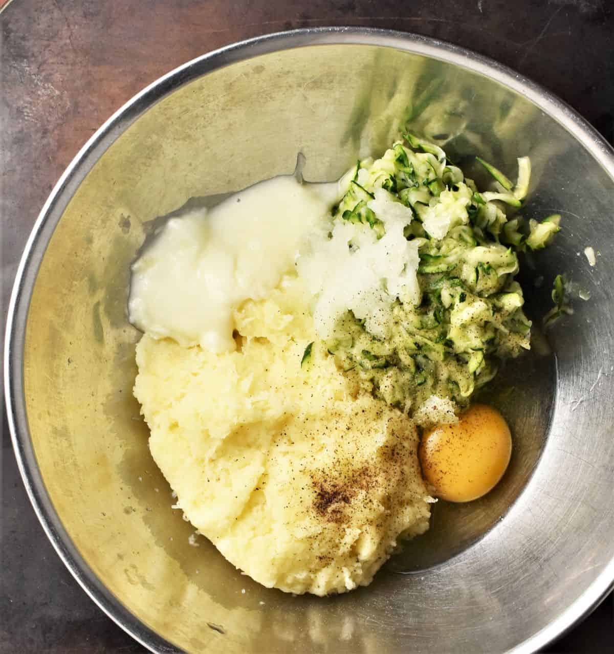 Zucchini potato fritters ingredients in metal bowl.