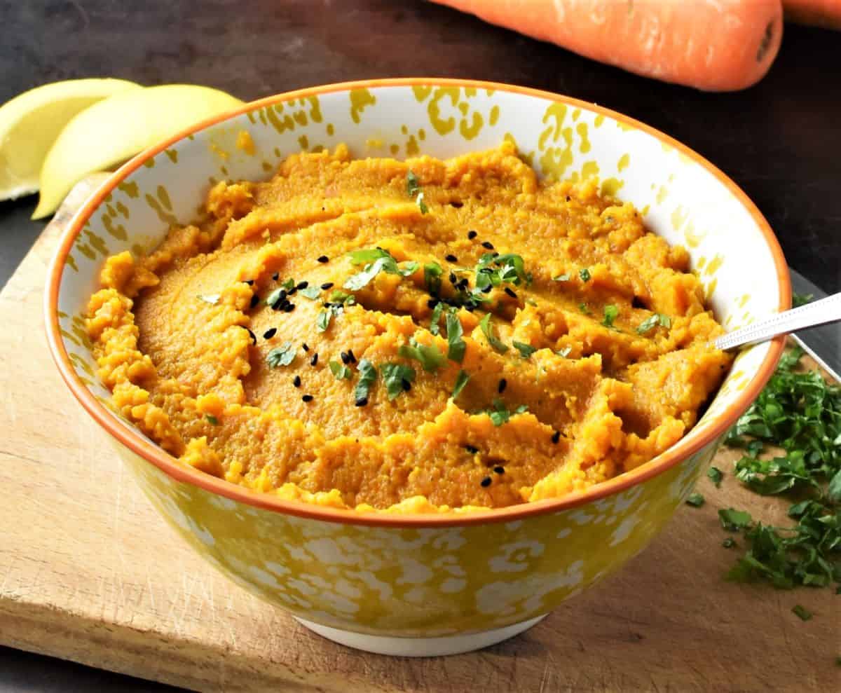 Side view of carrot puree in yellow bowl with spoon.