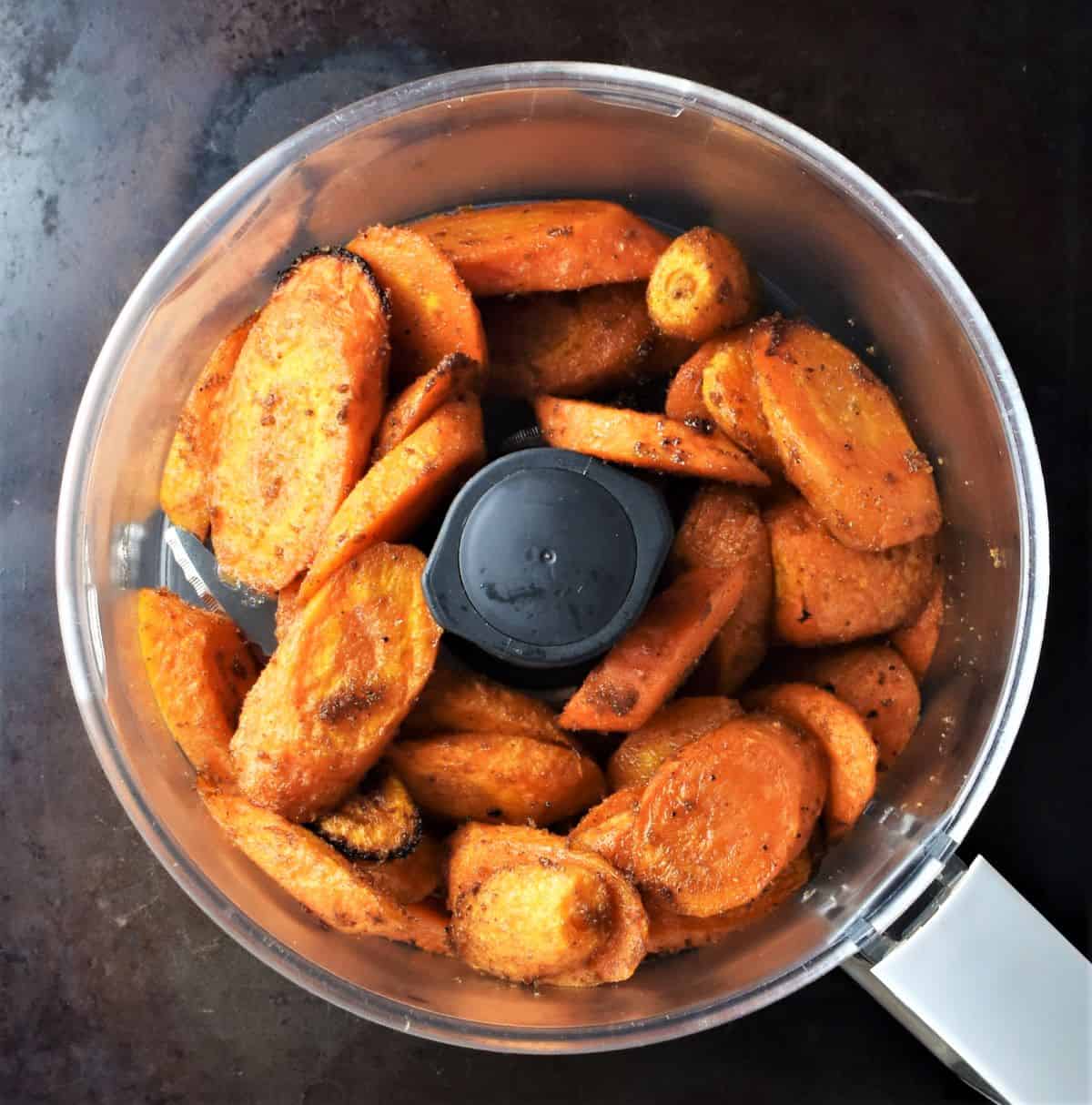 Sliced carrots with spices in food processor bowl.