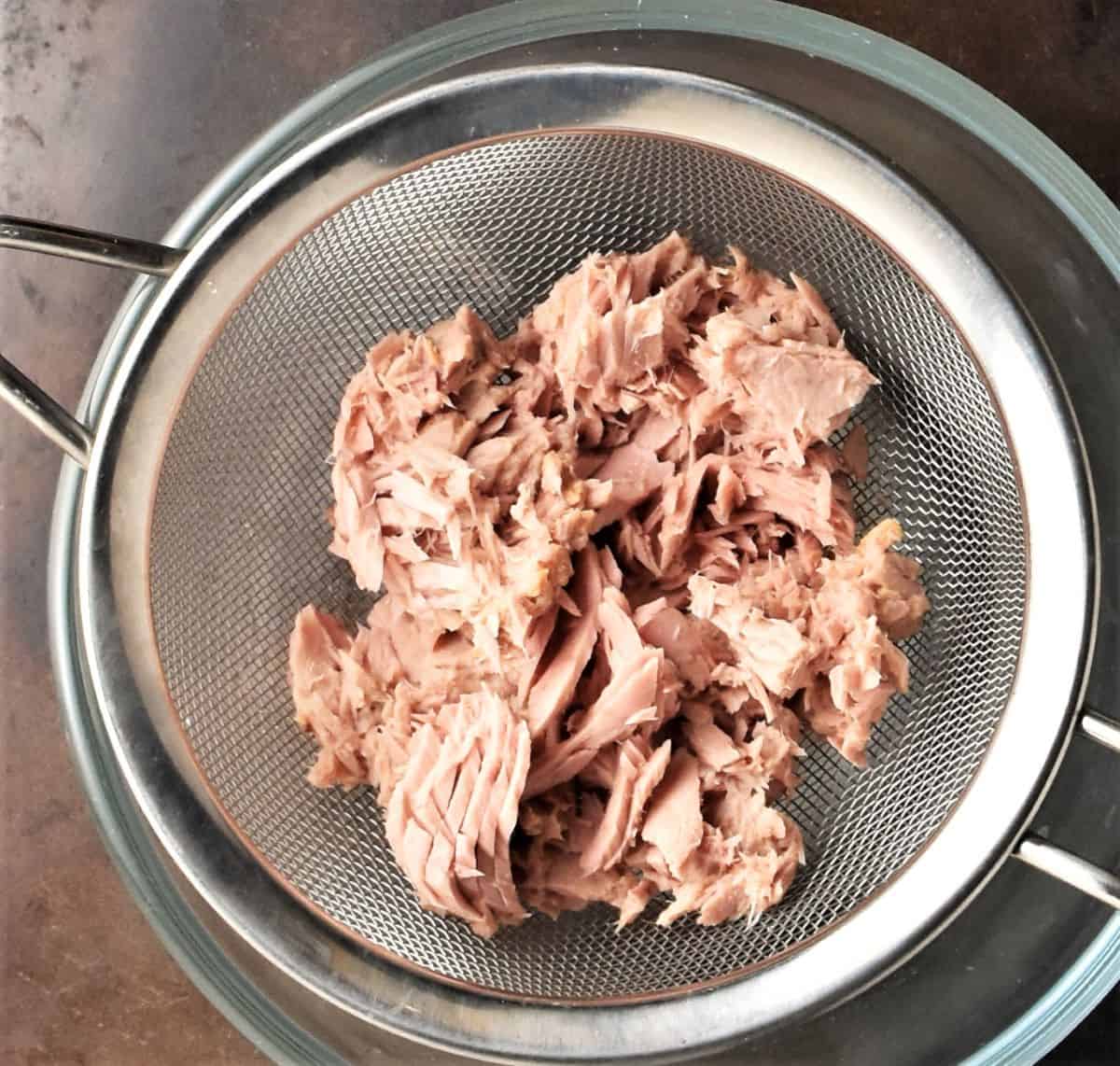 Canned tuna in sieve over bowl.