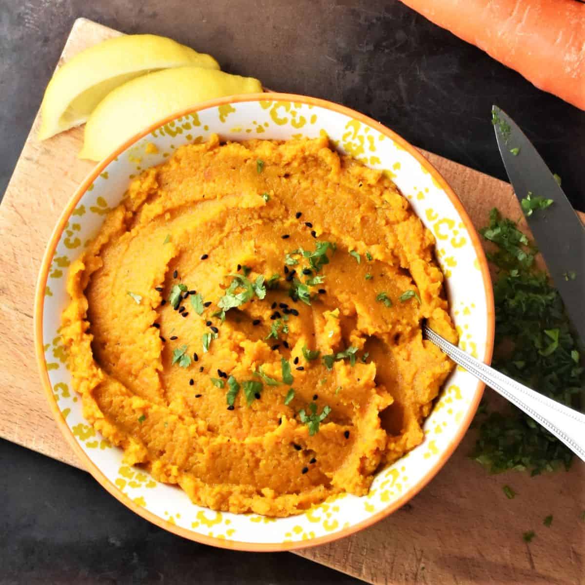 Top down view of mashed carrots in yellow bowl with spoon.