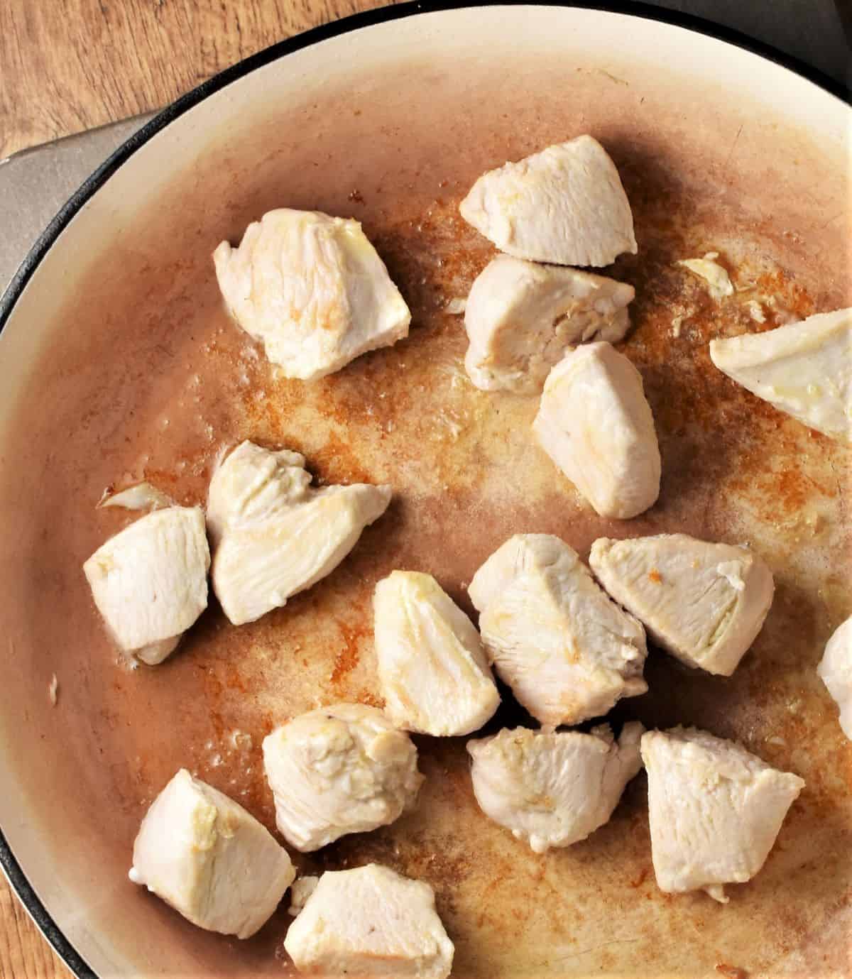 Searing chunks of chicken in large shallow pan.