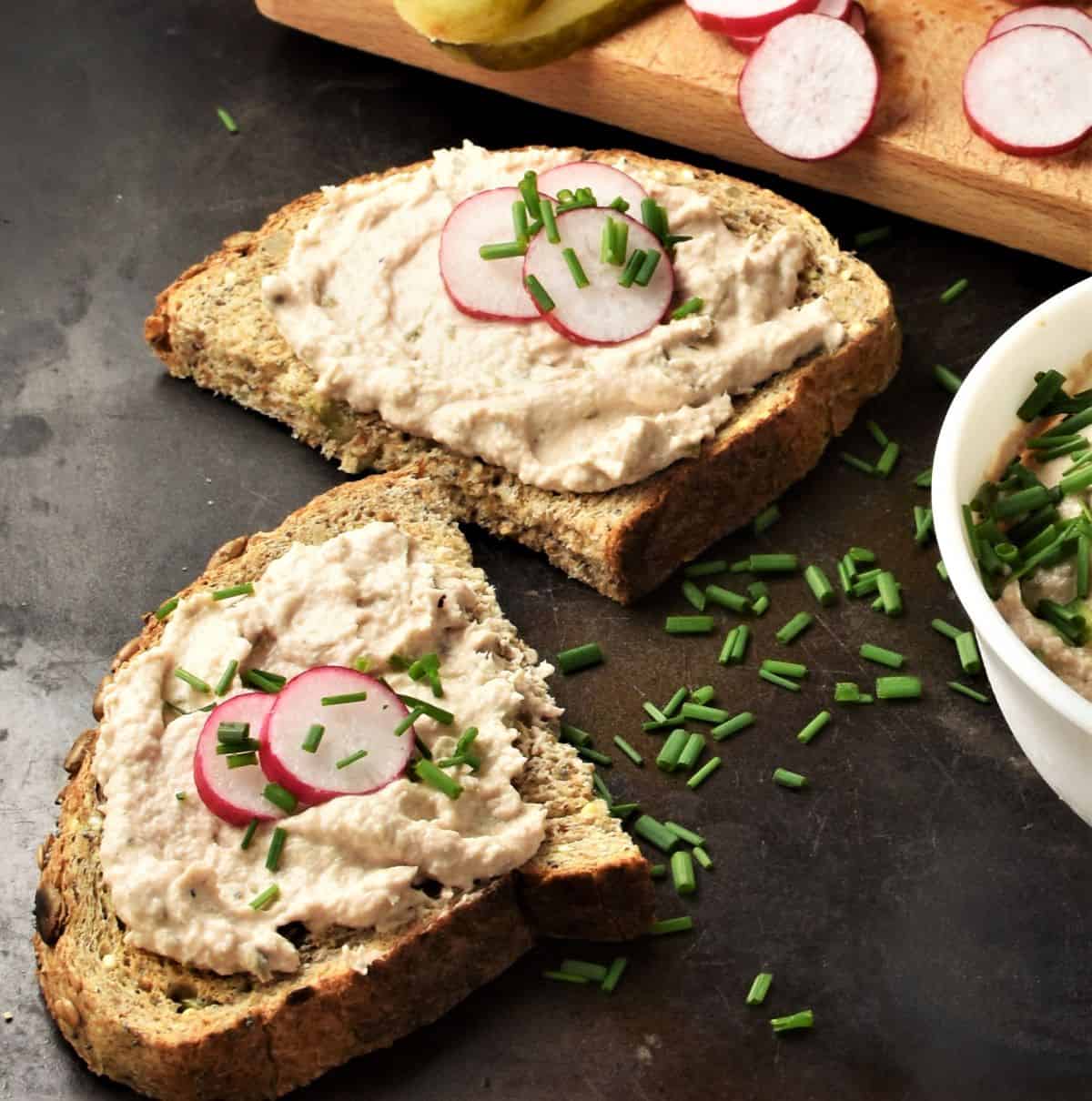 Side view of tuna pate on 2 slices of bread with sliced radish and chives.