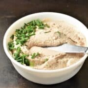 Side view of creamy tuna spread with chives and knife in white bowl.