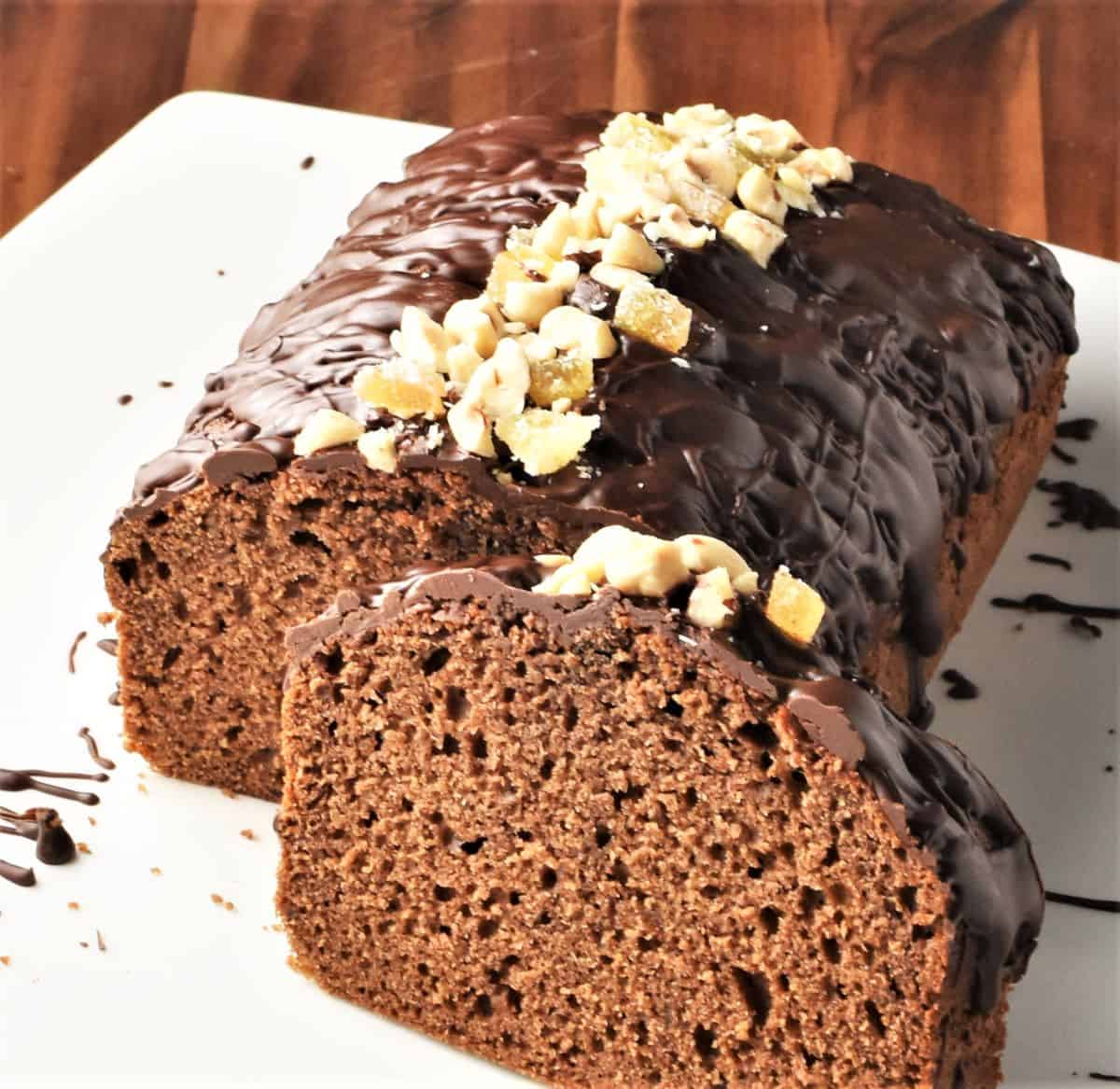 Side view of gingerbread loaf cake with chocolate drizzle and crushed nuts on top.