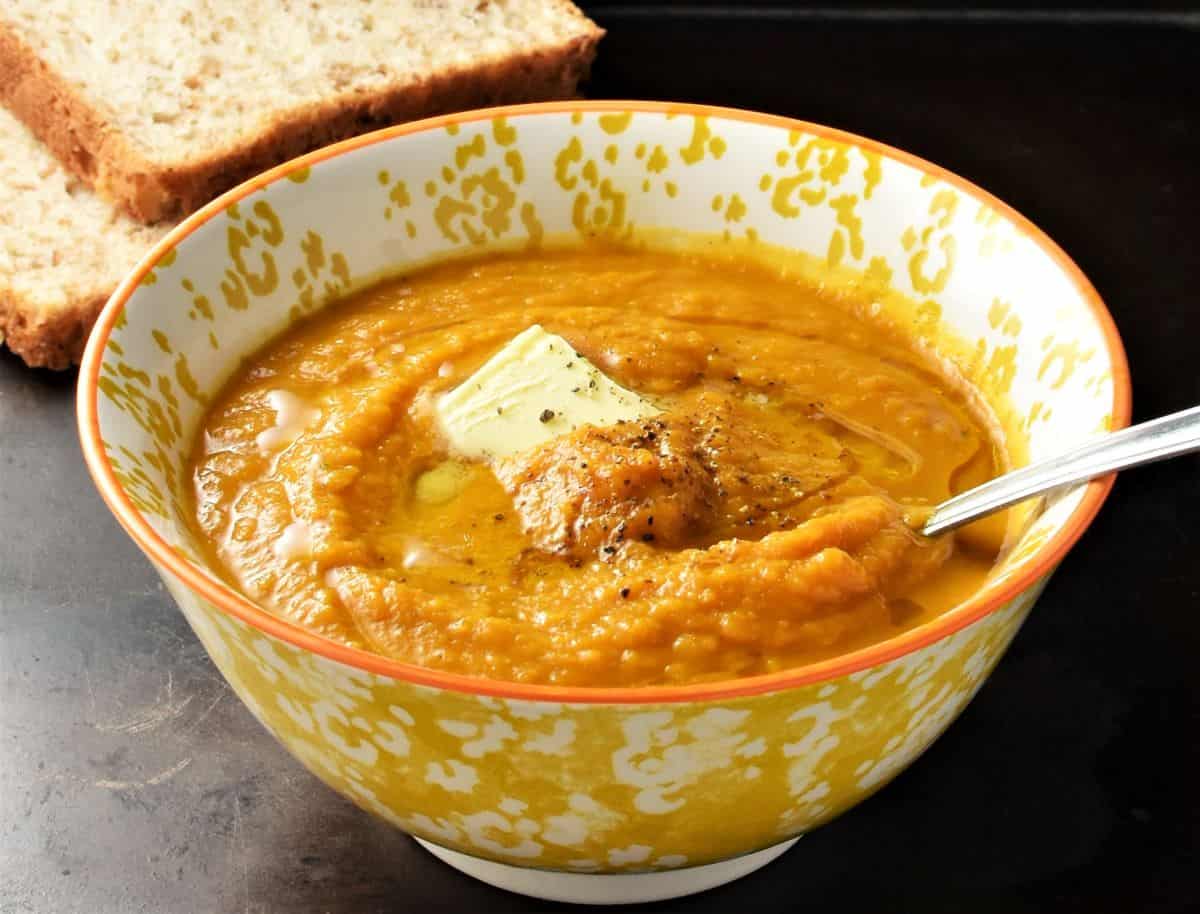 Side view of creamy carrot pumpkin soup in yellow bowl with spoon.