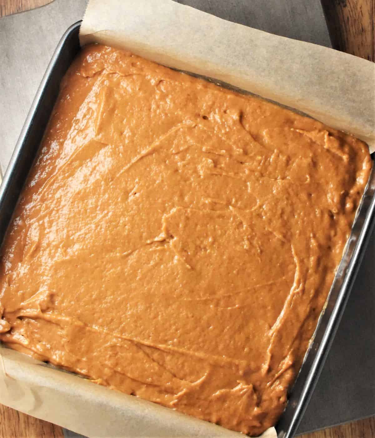Pumpkin cake batter in square pan lined with parchment.