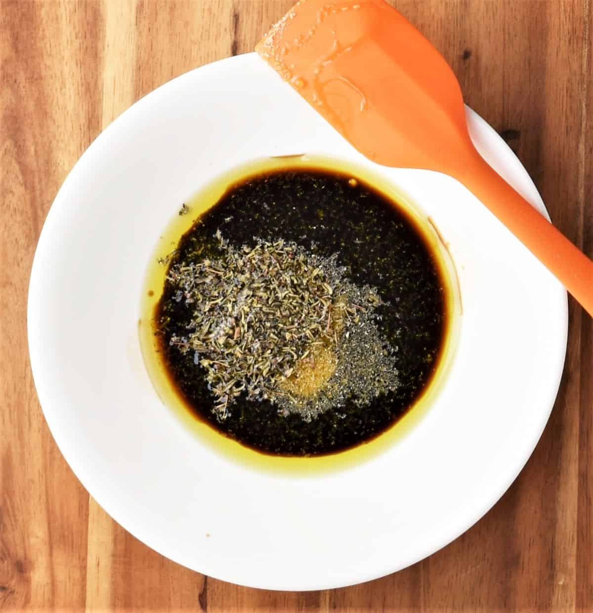 Balsamic dressing in white bowl with orange spatula.