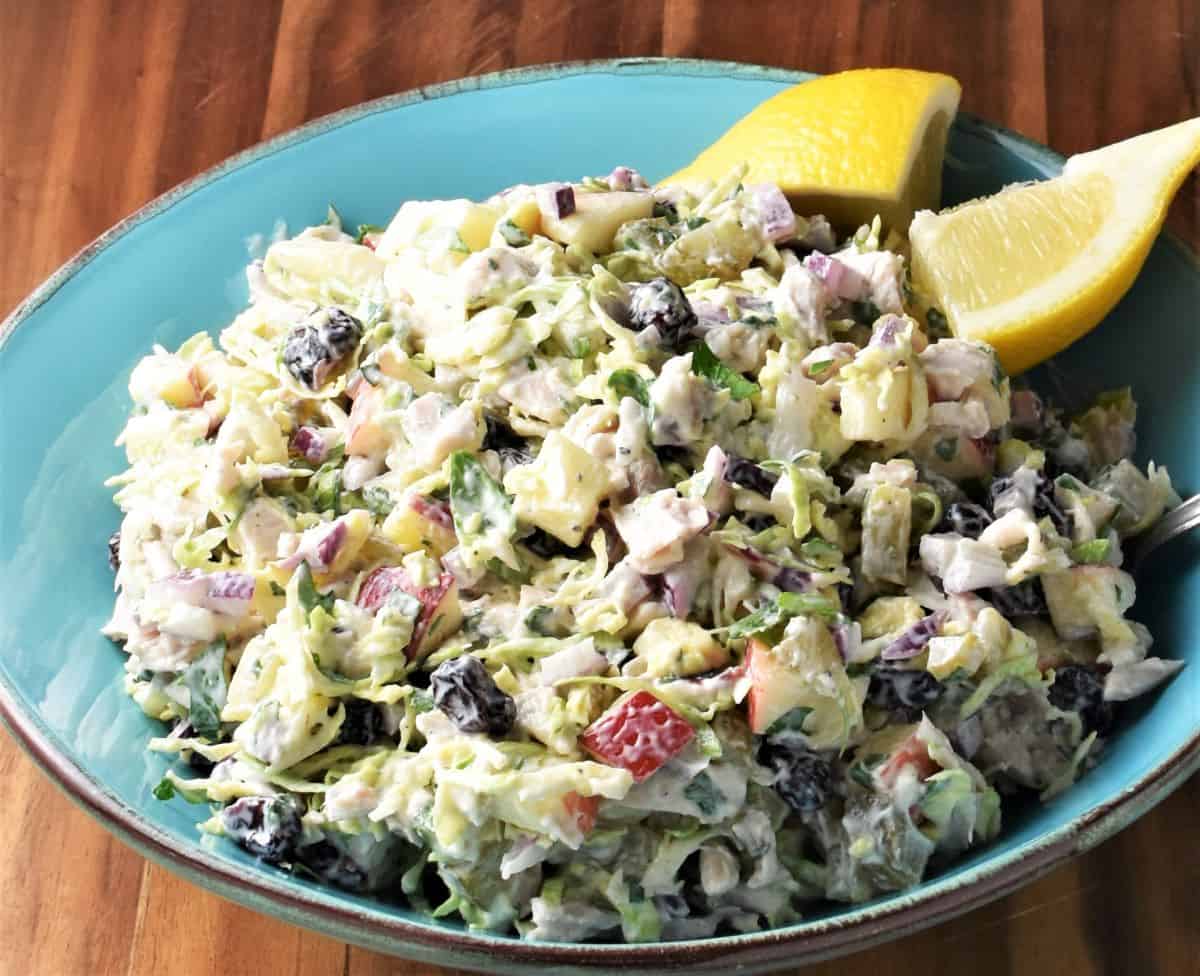 Side view of turkey and cranberry salad in blue bowl with lemon wedges.