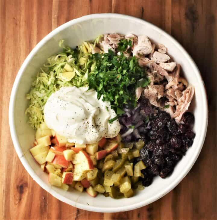 Ingredients for cranberry and turkey salad in large white bowl.
