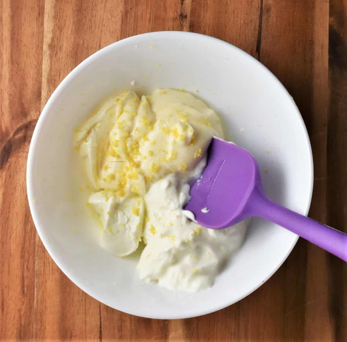 Creamy salad dressing ingredients in white bowl with purple spoon.