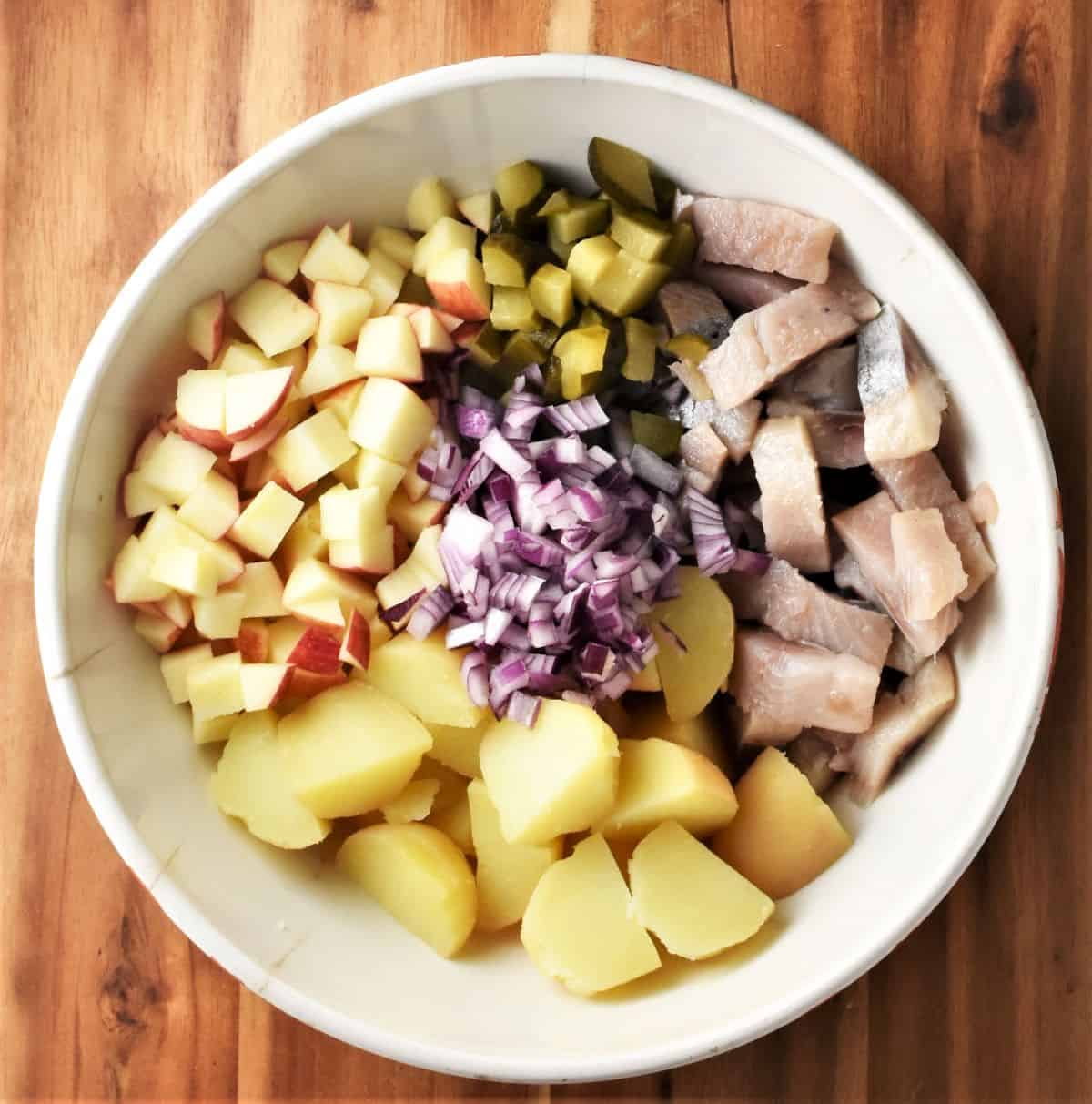 Chopped ingredients in large white bowl for making herring salad.