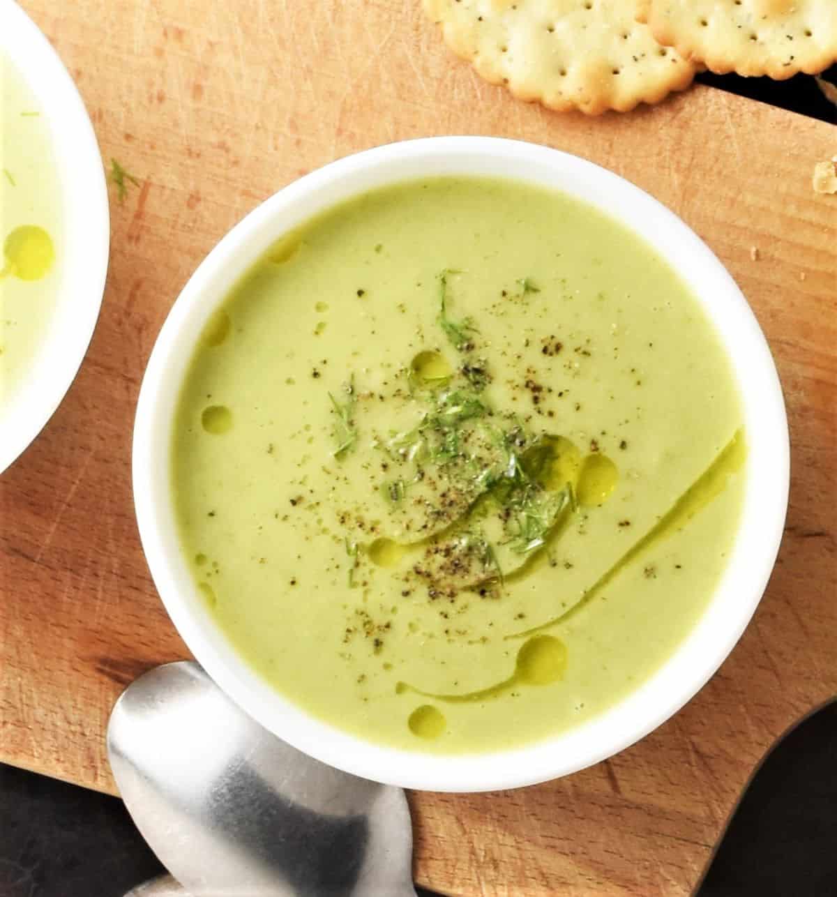 Top down view of cream of brussels sprout soup in white bowl and crackers in background.