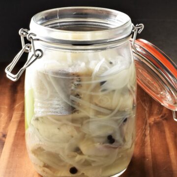 Close-up view of pickled herring with onion and spices in open jar.