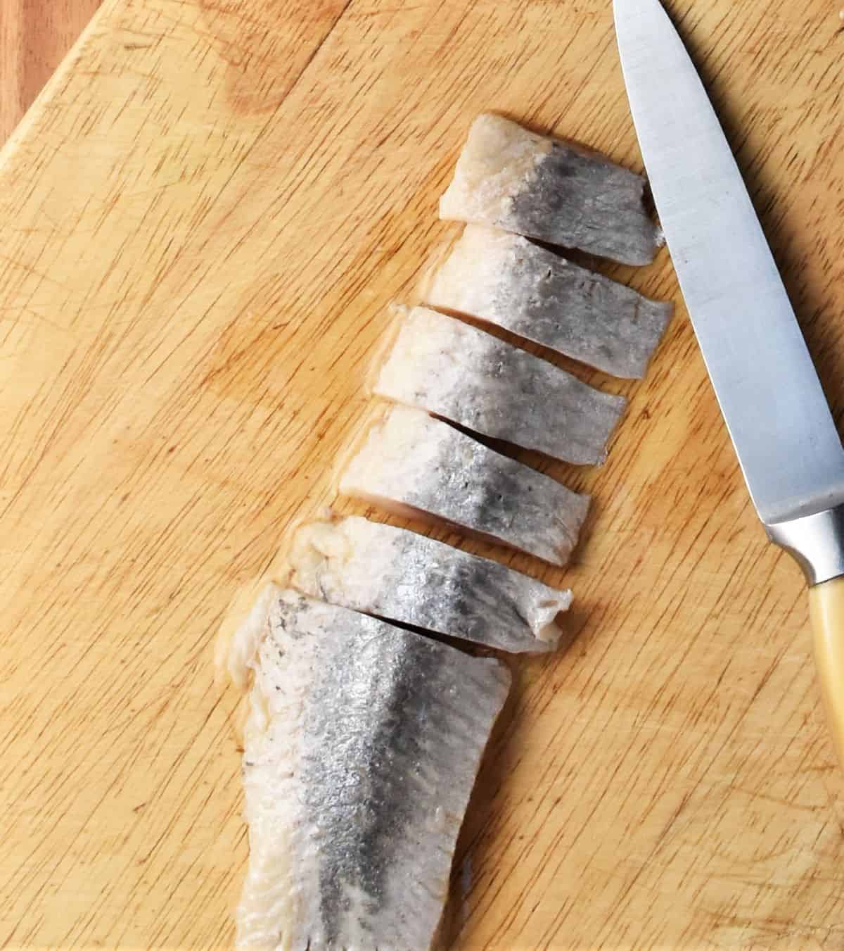 Chopping herring fillet on top of wooden board.