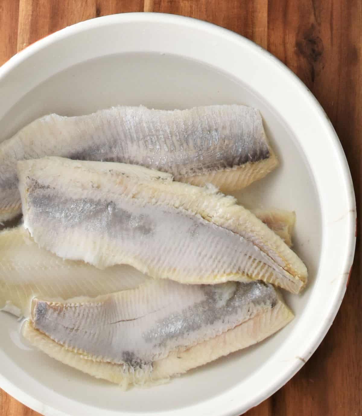 4 fillets of herring soaking in water in bowl.