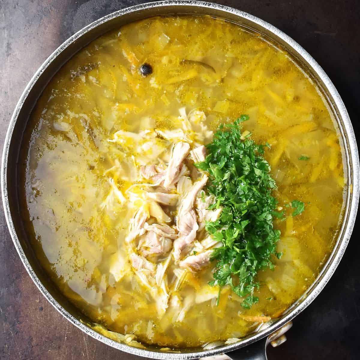 Top down view of Polish ogorkowa pickled soup with shredded chicken and parsley in large pot.