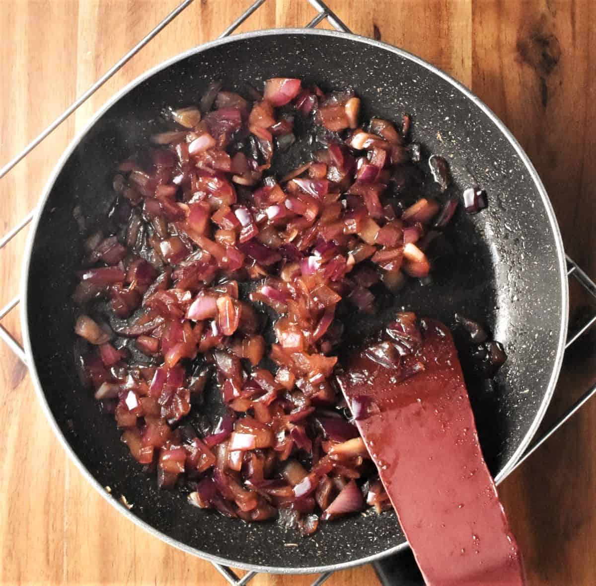 Frying chopped red onion in pan with red spatula.