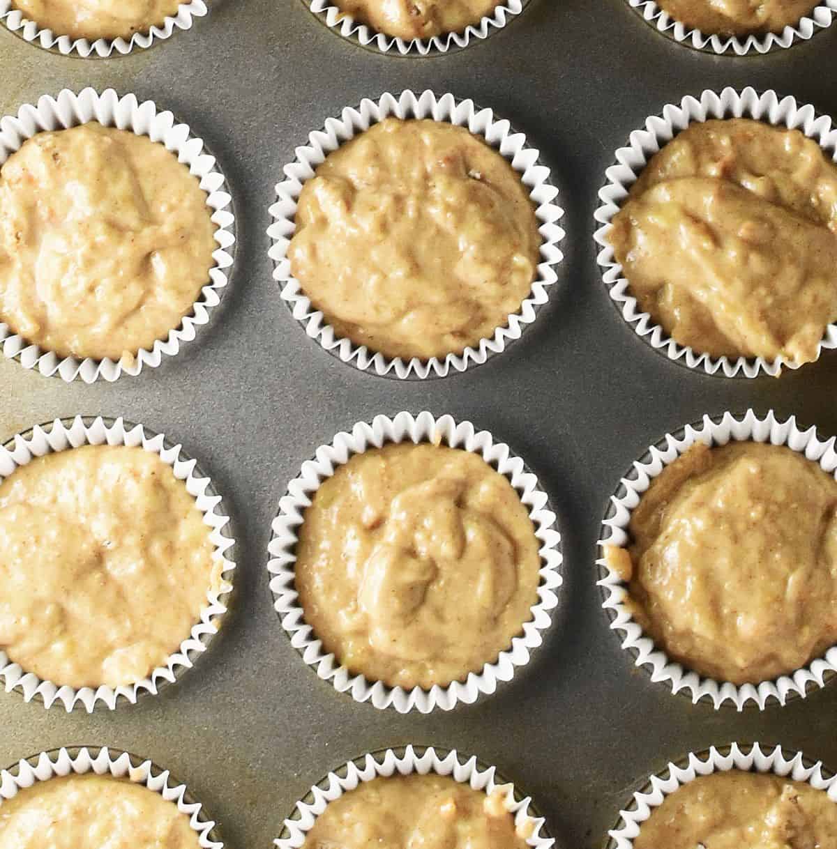 Banana peanut butter muffin batter in white paper cases in muffin pan.